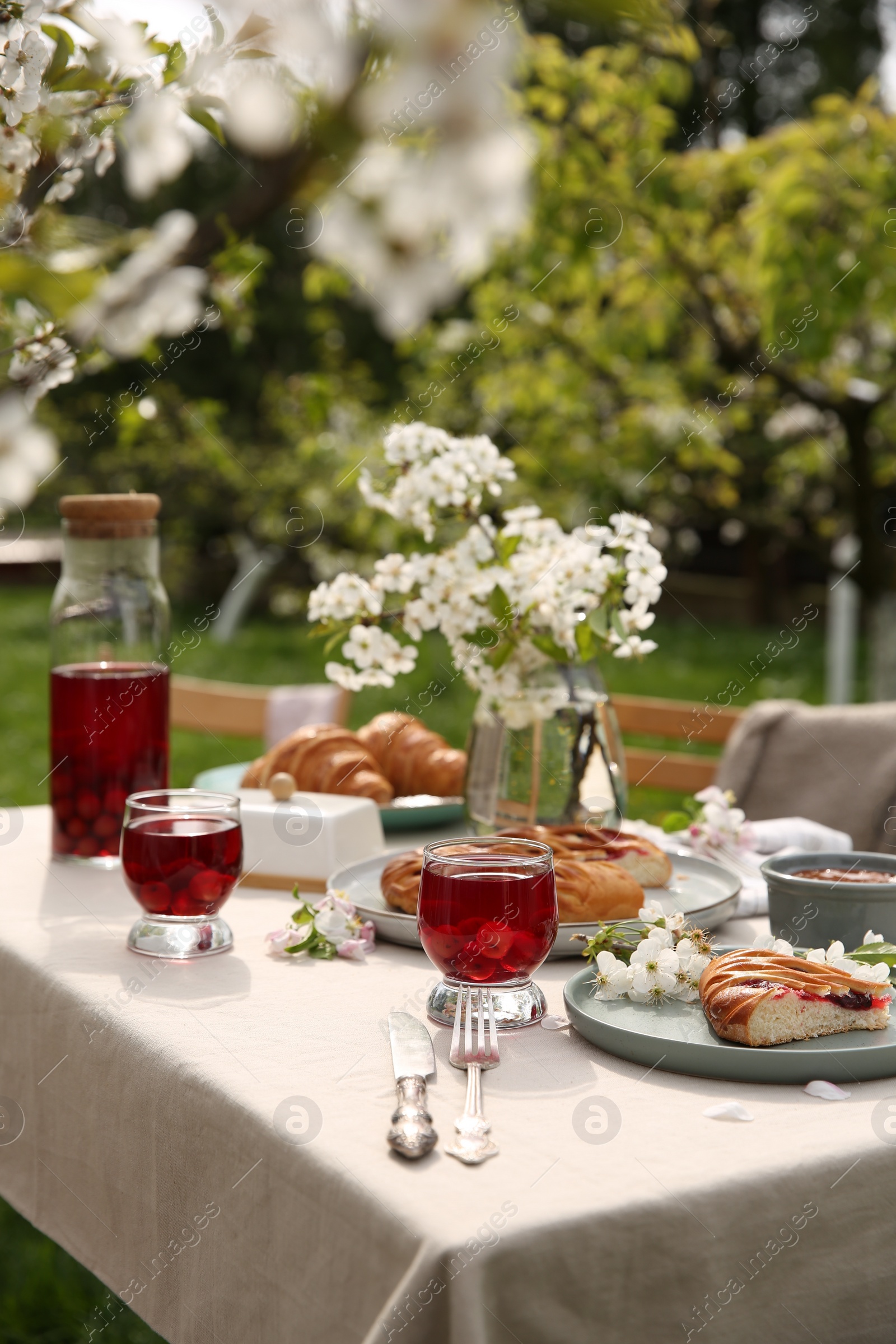 Photo of Stylish table setting with beautiful spring flowers, fruit drink and pie in garden