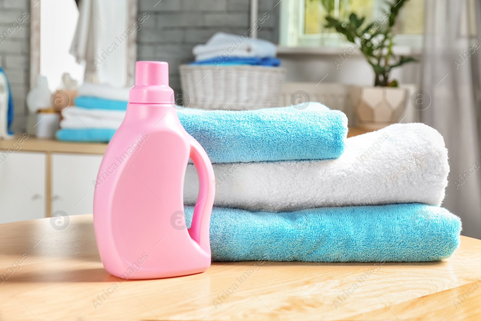 Photo of Stack of clean towels and bottle with detergent on table