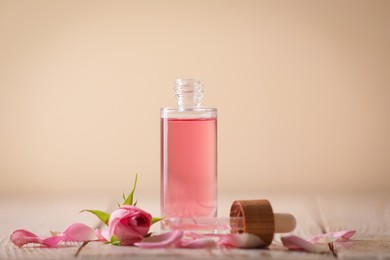 Bottle of essential rose oil and flowers on white wooden table against beige background