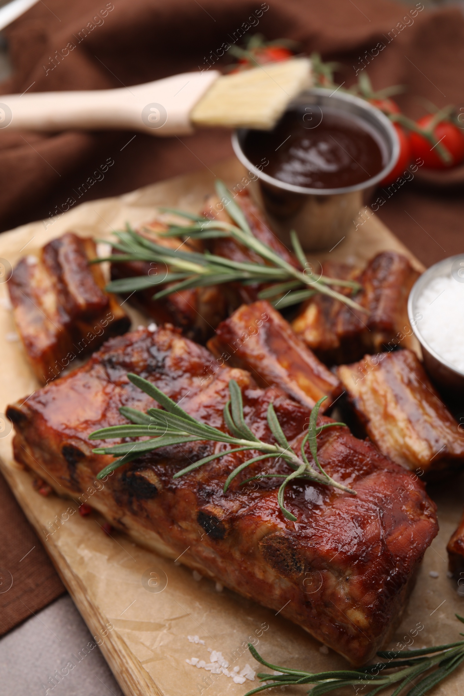 Photo of Tasty roasted pork ribs served with sauce and rosemary on brown table, closeup