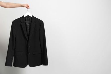 Photo of Woman holding hanger with black jacket near white wall, closeup. Space for text