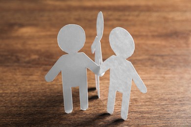 Photo of Teamwork concept. Paper figures of people holding hands on wooden table, closeup