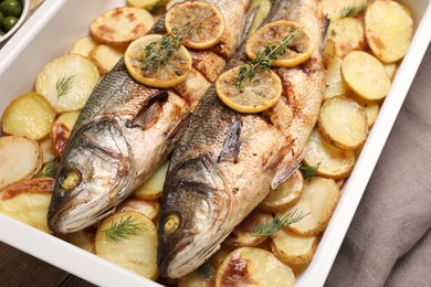 Photo of Baking tray with delicious baked sea bass fish and potatoes, closeup
