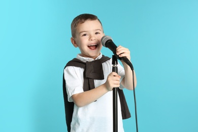 Cute funny boy with microphone on color background