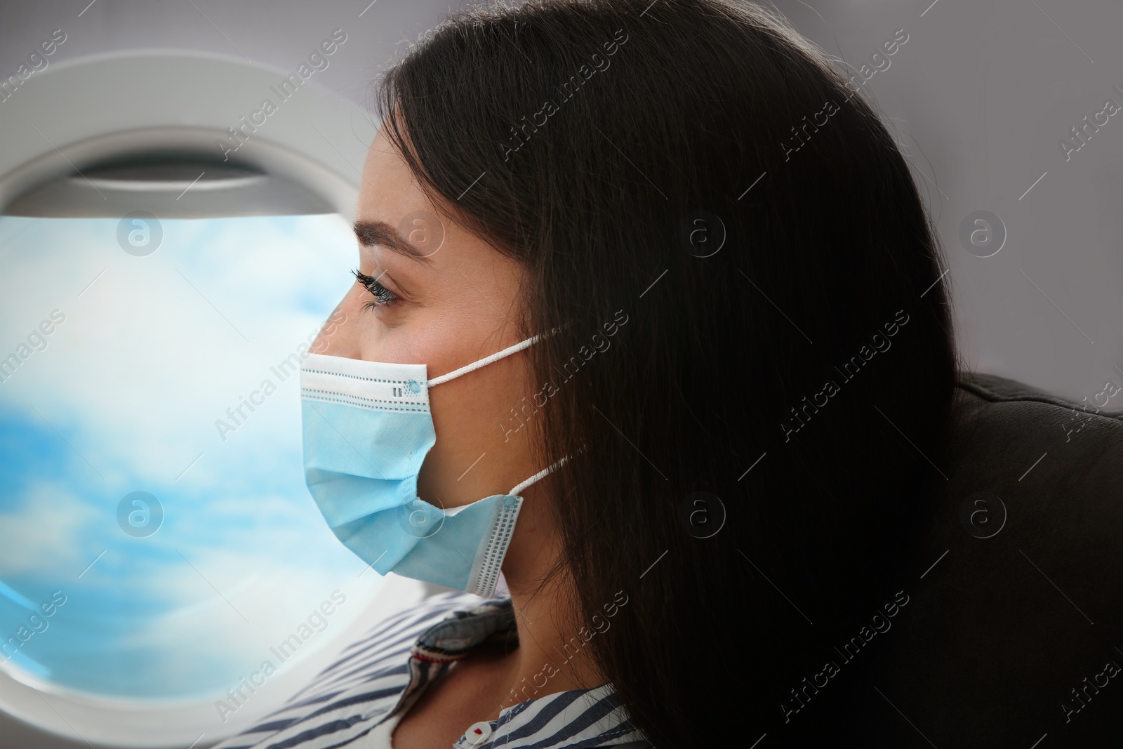 Image of Traveling by airplane during coronavirus pandemic. Woman with face mask near porthole