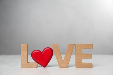 Photo of Word Love made of wooden letters and red decorative heart on light table