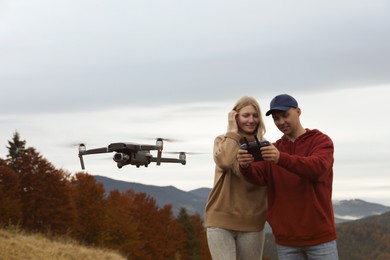 Photo of Young couple operating modern drone with remote control in mountains