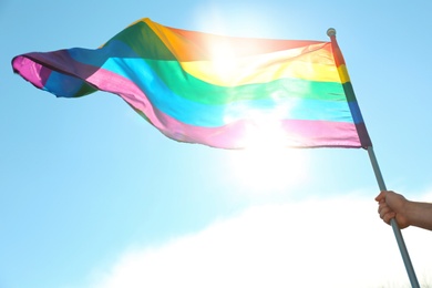 Gay man holding rainbow LGBT flag against blue sky