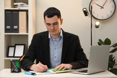 Photo of Man taking notes at table in office