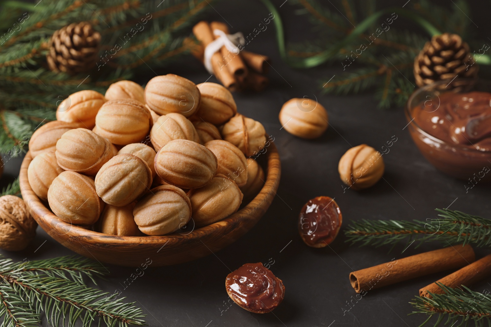 Photo of Homemade walnut shaped cookies with boiled condensed milk, cinnamon sticks and fir branches on black table