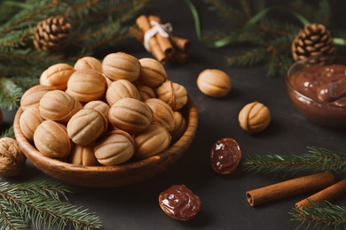 Homemade walnut shaped cookies with boiled condensed milk, cinnamon sticks and fir branches on black table