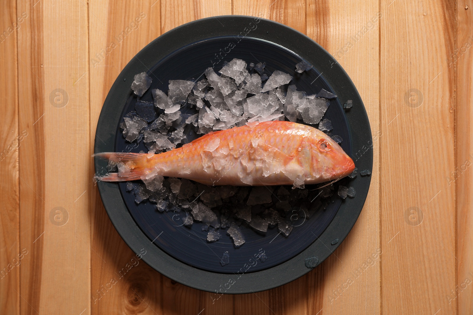 Photo of Fresh raw fish with ice on wooden table, top view