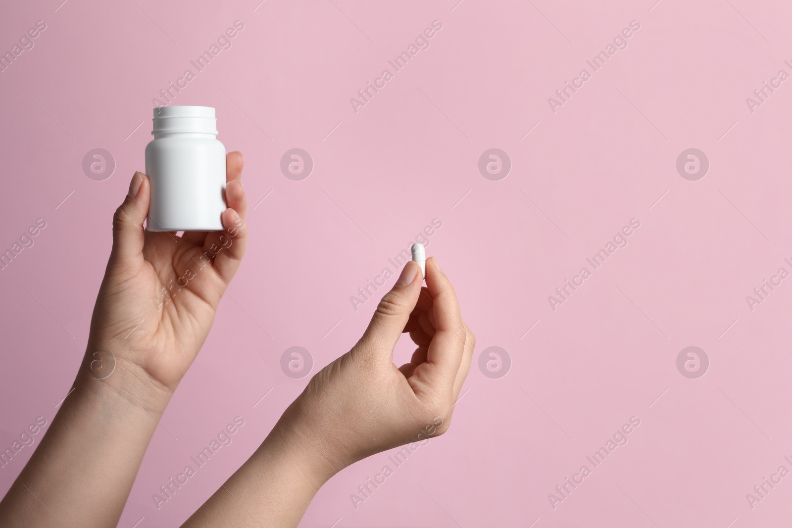 Photo of Woman holding pill and bottle on pink background, closeup. Space for text