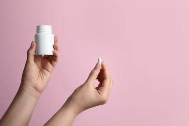 Woman holding pill and bottle on pink background, closeup. Space for text