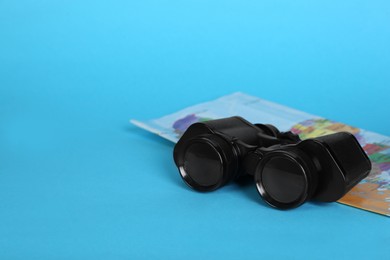 Modern binoculars and map on light blue background, space for text