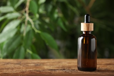 Bottle of essential oil on wooden table against blurred background, space for text