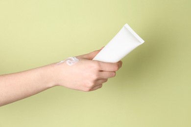 Woman with tube of cream on green background, closeup