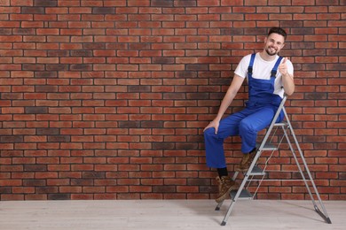 Photo of Happy worker showing thumb up near stepladder against brick wall, space for text