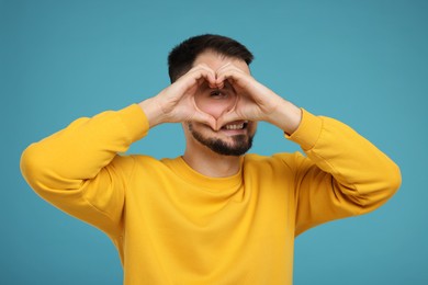 Man looking through folded in shape of heart hands on light blue background
