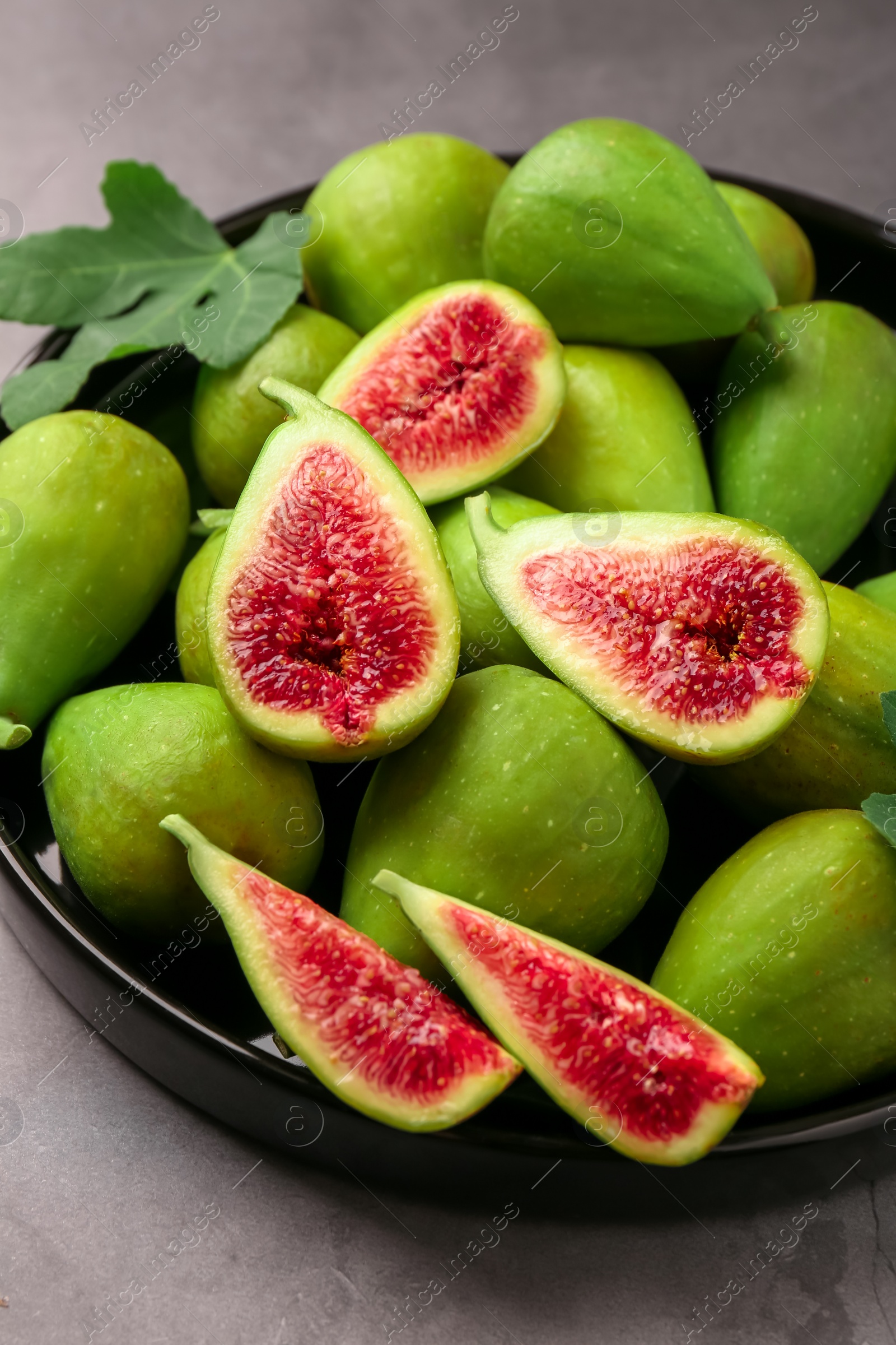 Photo of Cut and whole green figs on light gray table, closeup