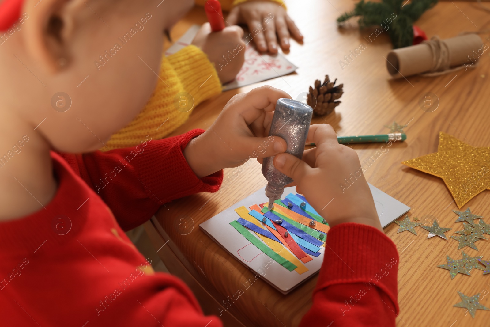 Photo of Cute little child making beautiful Christmas greeting card at wooden table, closeup