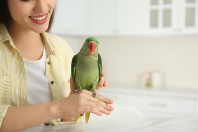 Photo of Young woman with Alexandrine parakeet indoors, closeup. Cute pet