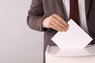 Man putting his vote into ballot box on light grey background, closeup. Space for text