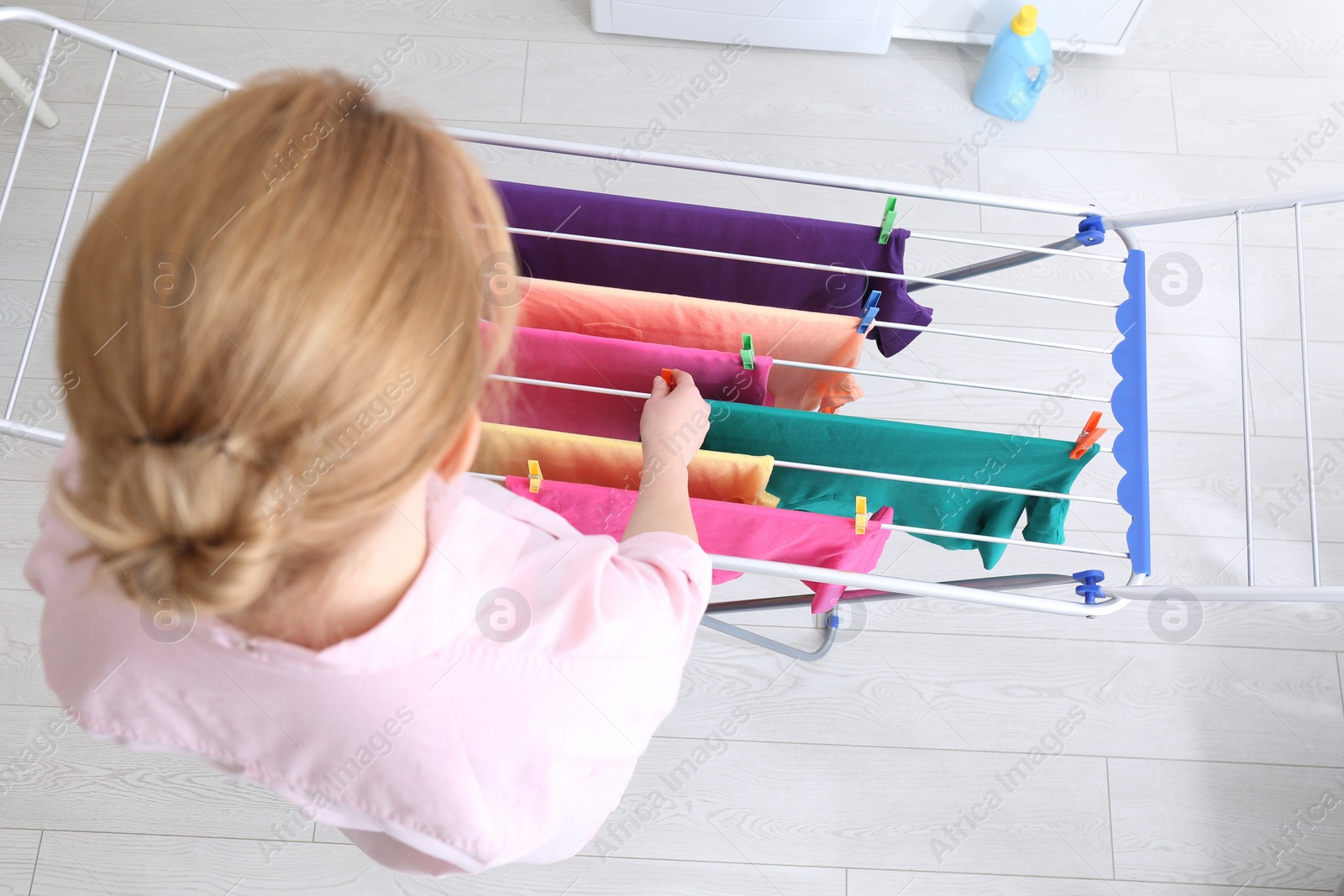 Photo of Woman hanging clean laundry on drying rack indoors, above view