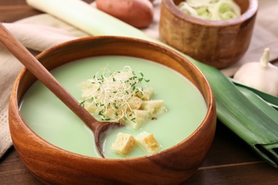 Photo of Bowl of tasty leek soup with croutons and spoon on wooden table, closeup