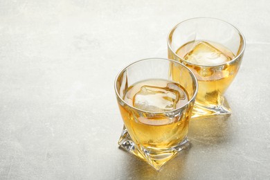 Photo of Tasty whiskey with ice in glasses on light table, closeup. Space for text