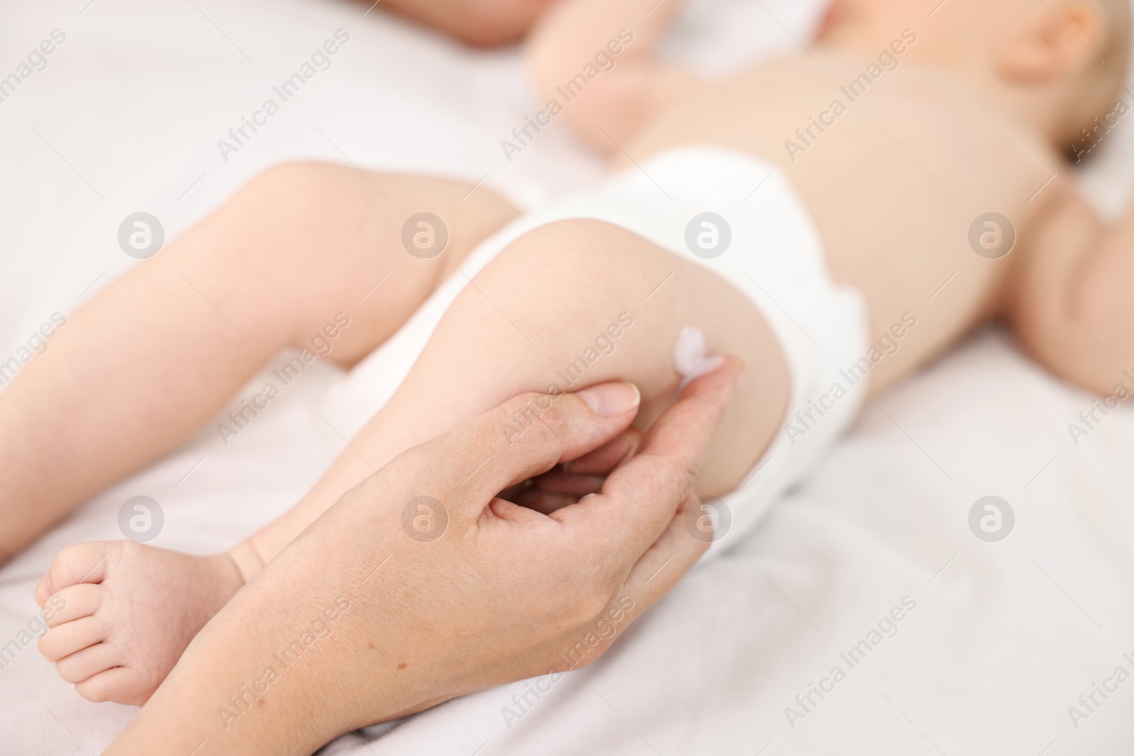 Photo of Woman applying body cream onto baby`s skin on bed, closeup