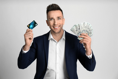 Happy man with cash money and credit card on light grey background