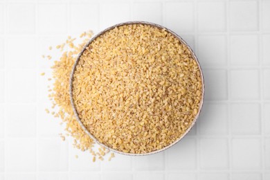 Photo of Raw bulgur in bowl on white tiled table, top view