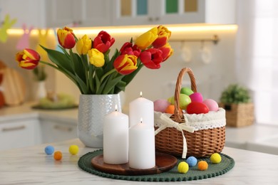 Photo of Easter decorations. Bouquet of tulips, painted eggs and burning candles on table indoors, closeup