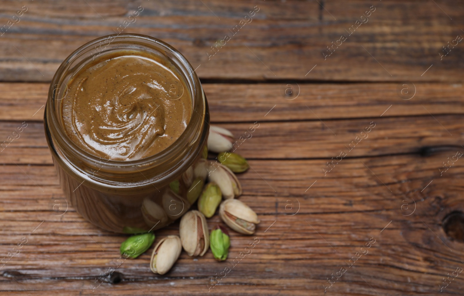 Photo of Tasty nut paste in jar and pistachios on wooden table, above view. Space for text