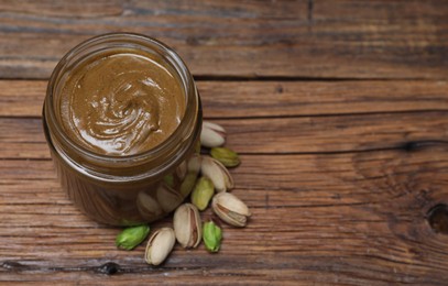 Tasty nut paste in jar and pistachios on wooden table, above view. Space for text