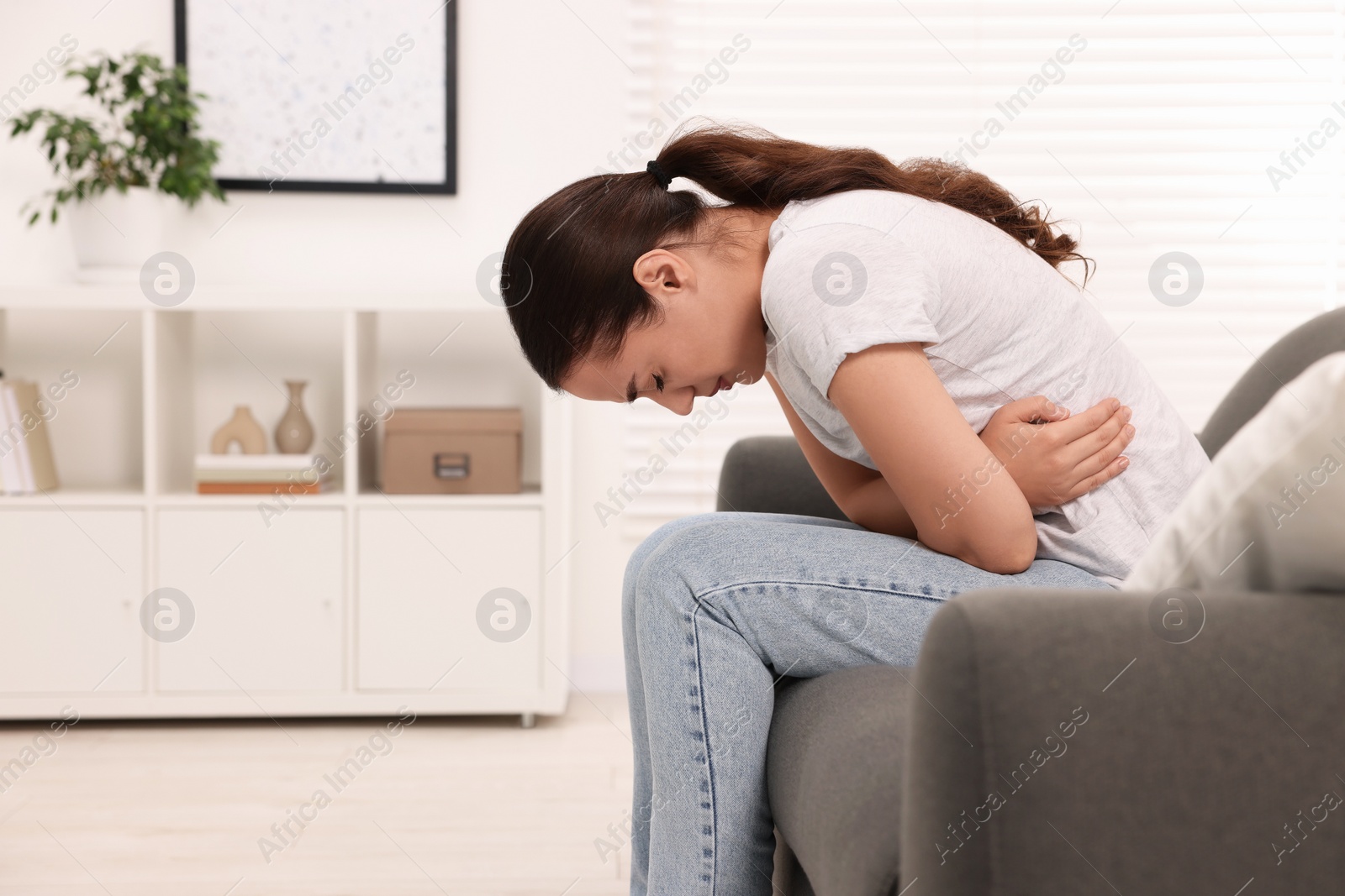 Photo of Woman suffering from abdominal pain on sofa at home. Unhealthy stomach