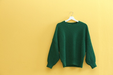 Hanger with stylish sweater on yellow wall