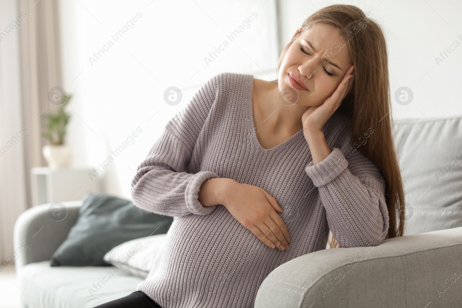 Photo of Young pregnant woman suffering from headache at home