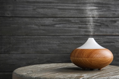 Photo of Modern essential oil diffuser on wooden table against dark background. Space for text