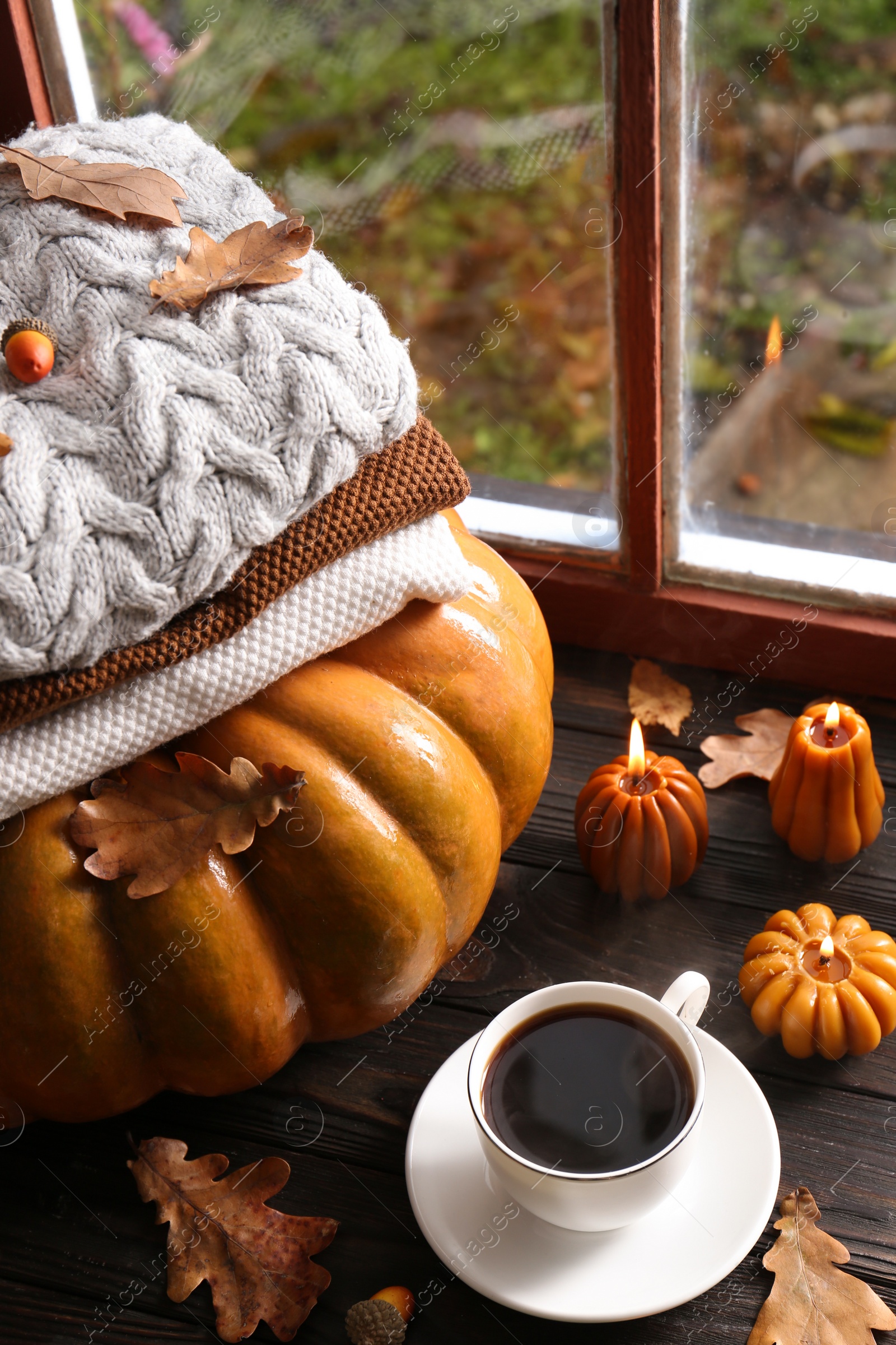 Photo of Cup of hot drink and pumpkin shaped candles on wooden table near window. Cozy autumn atmosphere