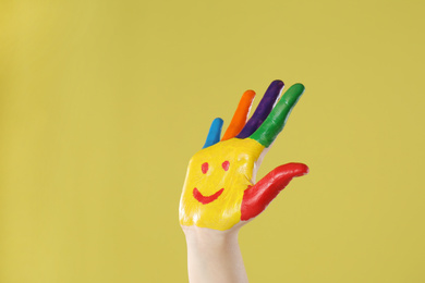 Photo of Kid with smiling face drawn on palm against yellow background, closeup