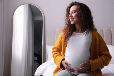 Pregnant young African-American woman sitting on bed at home