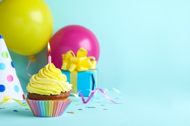 Photo of Delicious birthday cupcake with candle, near gift box and party hat on light blue background, space for text