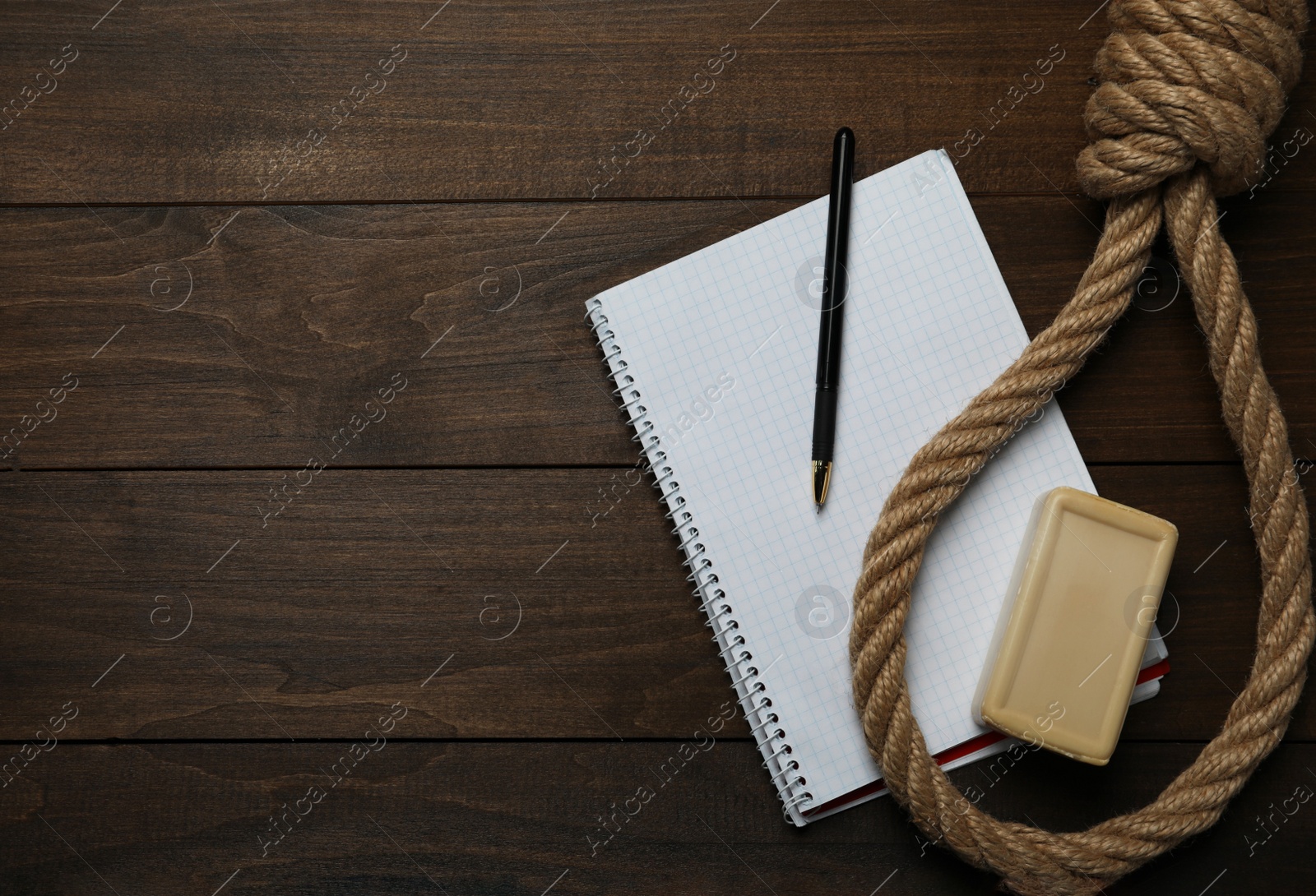 Photo of Rope noose, soap bar and blank notebook with pen on wooden table, flat lay. Space for text