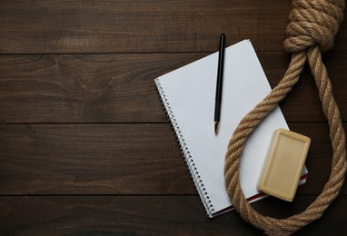 Photo of Rope noose, soap bar and blank notebook with pen on wooden table, flat lay. Space for text