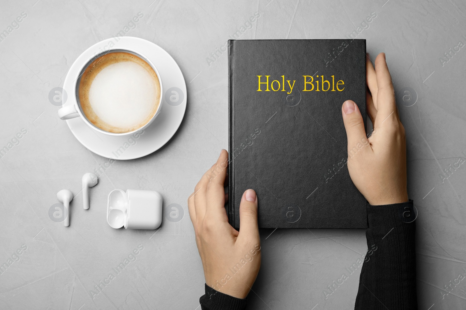 Photo of Woman with Bible, cup of coffee and earphones at light grey table, top view. Religious audiobook