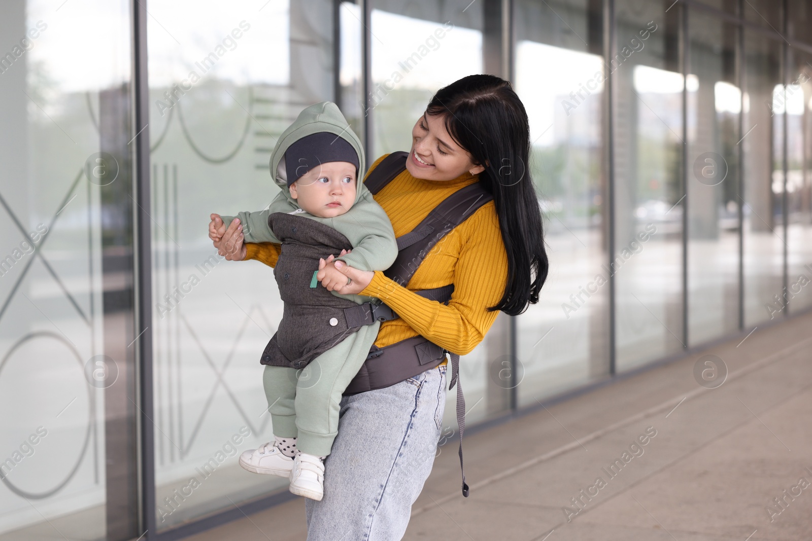 Photo of Mother holding her child in sling (baby carrier) near building outdoors