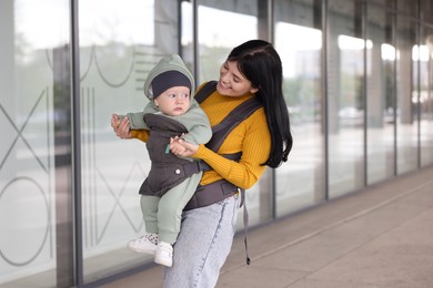 Mother holding her child in sling (baby carrier) near building outdoors