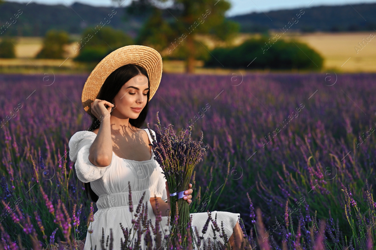 Photo of Beautiful young woman with bouquet sitting in lavender field